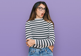 Young beautiful teen girl wearing casual clothes and glasses afraid and shocked with surprise expression, fear and excited face.