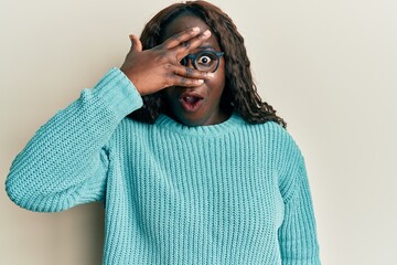 African young woman wearing casual clothes and glasses peeking in shock covering face and eyes with hand, looking through fingers afraid