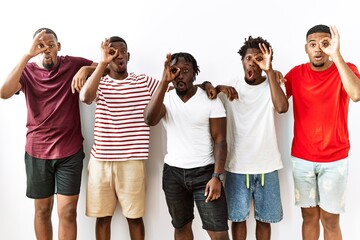 Obraz premium Young african group of friends standing together over isolated background doing ok gesture shocked with surprised face, eye looking through fingers. unbelieving expression.