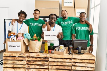 Group of young african american volunteers smiling happy and hugging holding donations banner at charity center.