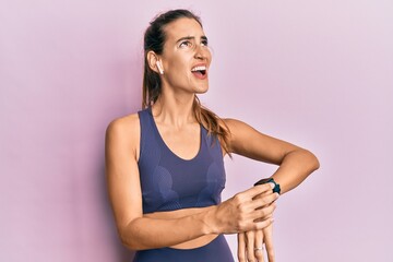 Young beautiful woman wearing gym clothes, using earphones and smart watch angry and mad screaming frustrated and furious, shouting with anger looking up.