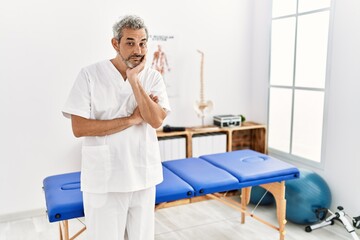 Fototapeta na wymiar Middle age hispanic therapist man working at pain recovery clinic thinking looking tired and bored with depression problems with crossed arms.