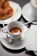 Traditional Italian breakfast. Fresh croissants with cream and sugar powder, espresso coffee and cappuccino on a black wooden table in Milan, Lombardy, Italy. European food and pastry.