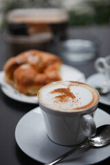 Traditional Italian breakfast. Fresh croissants with cream and sugar powder, espresso coffee and cappuccino on a black wooden table in Milan, Lombardy, Italy. European food and pastry.