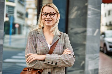 Fototapeta premium Young blonde businesswoman smiling happy with arms crossed gesture at the city.