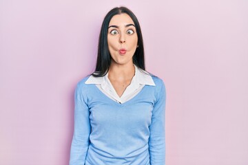 Fototapeta premium Beautiful woman with blue eyes standing over pink background making fish face with lips, crazy and comical gesture. funny expression.