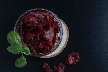 Jerky beef, jerky in a glass bowl on a dark background. Rustic country style dried meat. Delicious...