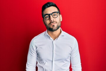 Young hispanic businessman wearing shirt and glasses relaxed with serious expression on face. simple and natural looking at the camera.