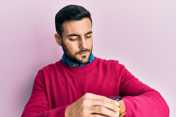 Young hispanic man wearing casual clothes checking the time on wrist watch, relaxed and confident