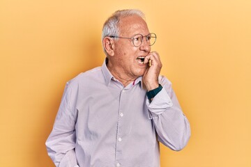 Senior man with grey hair wearing elegant shirt and glasses looking stressed and nervous with hands on mouth biting nails. anxiety problem.