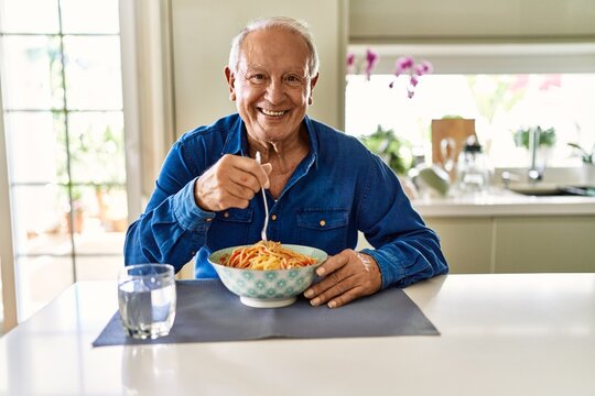 Senior Man With Grey Hair Eating Pasta Spaghetti At Home With A Happy And Cool Smile On Face. Lucky Person.