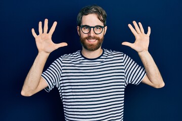 Caucasian man with beard wearing striped t shirt and glasses showing and pointing up with fingers number ten while smiling confident and happy.