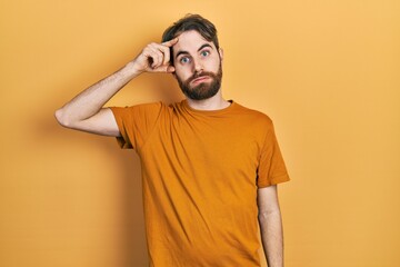 Caucasian man with beard wearing casual yellow t shirt worried and stressed about a problem with hand on forehead, nervous and anxious for crisis