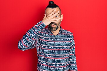 Young hispanic man wearing casual clothes peeking in shock covering face and eyes with hand, looking through fingers afraid