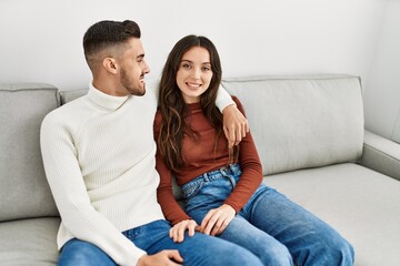 Young hispanic couple sitting on the sofa and hugging at home.