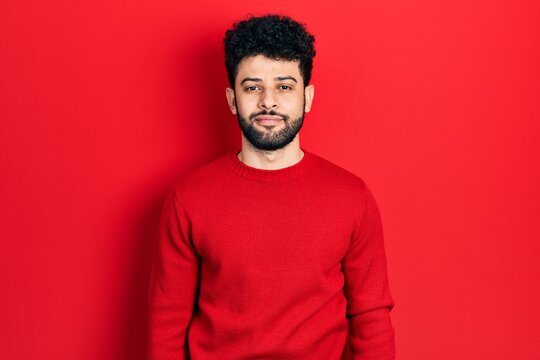 Young arab man with beard wearing casual red sweater relaxed with serious expression on face. simple and natural looking at the camera.