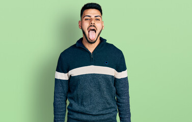 Young hispanic man with beard wearing casual winter sweater sticking tongue out happy with funny expression. emotion concept.