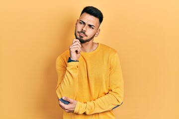 Young hispanic man with beard wearing casual winter sweater thinking concentrated about doubt with finger on chin and looking up wondering