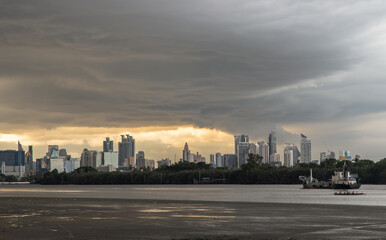 Bangkok, Thailand - 17 Jul 2021 : A cargo ship is sailing in the Chao Phraya River at evening with green forest and skyscrapers at the background. Copy space, Selective focus.