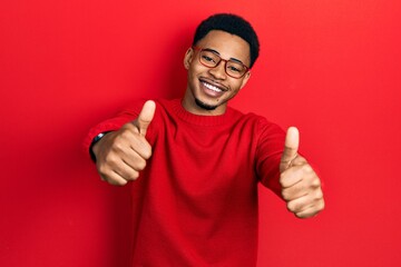 Young african american man wearing casual clothes and glasses approving doing positive gesture with hand, thumbs up smiling and happy for success. winner gesture.