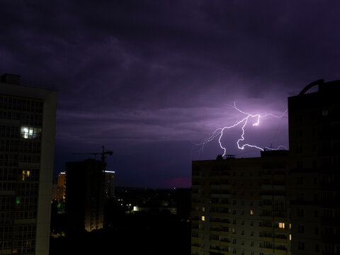 Several lightning bolts in one shot against the background of the city district of high-rise buildings. Storm with a thunderstorm in the night. Composite photo with a long exposure.