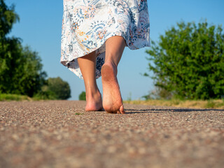 A woman dressed in a dress walks barefoot on the asphalt. Rear view. The concept of travel,...