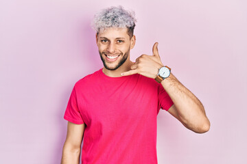 Young hispanic man with modern dyed hair wearing casual pink t shirt smiling doing phone gesture with hand and fingers like talking on the telephone. communicating concepts.