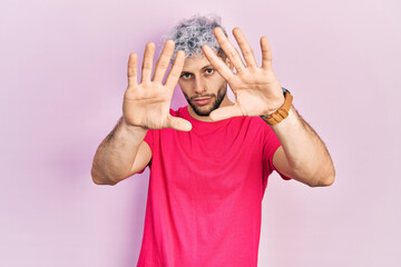 Young hispanic man with modern dyed hair wearing casual pink t shirt doing frame using hands palms and fingers, camera perspective