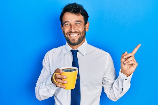 Handsome business man with beard drinking a cup coffee smiling happy pointing with hand and finger to the side
