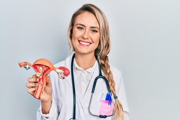 Beautiful young blonde woman holding anatomical model of female genital organ looking positive and...