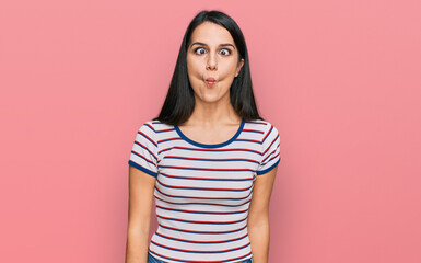 Young hispanic girl wearing casual striped t shirt making fish face with lips, crazy and comical gesture. funny expression.