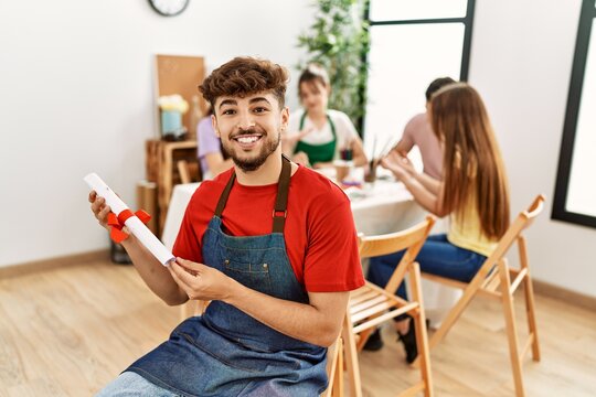 Group of people drawing sitting on the table. Young man smiling happy holding diploma at art studio.