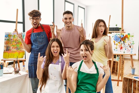 Group of five hispanic artists at art studio shouting with crazy expression doing rock symbol with hands up. music star. heavy concept.
