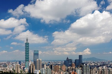 Obraz premium Aerial panorama of Downtown Taipei, vibrant capital city of Taiwan, with prominent Taipei 101 Tower among skyscrapers in Xinyi District & Yangmingshan Mountain on distant horizon under blue sunny sky