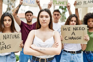 Young activist woman with arms crossed gesture standing with a group of protesters holding protest...