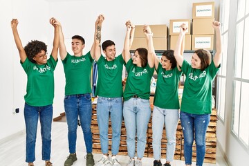 Group of young volunteers smiing happy with hands raised up at charity center.