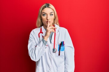 Young caucasian woman wearing doctor uniform and stethoscope asking to be quiet with finger on...