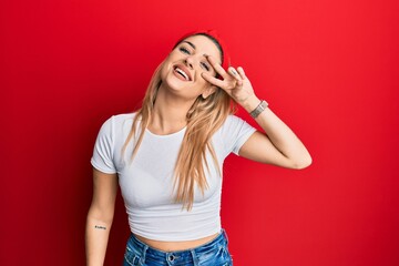 Young caucasian woman wearing casual white t shirt doing peace symbol with fingers over face, smiling cheerful showing victory