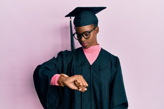 Young african american girl wearing graduation cap and ceremony robe checking the time on wrist watch, relaxed and confident