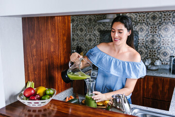 Latin Woman making green smoothie or Detox juice in kitchen at Home in healthy eating concept in...