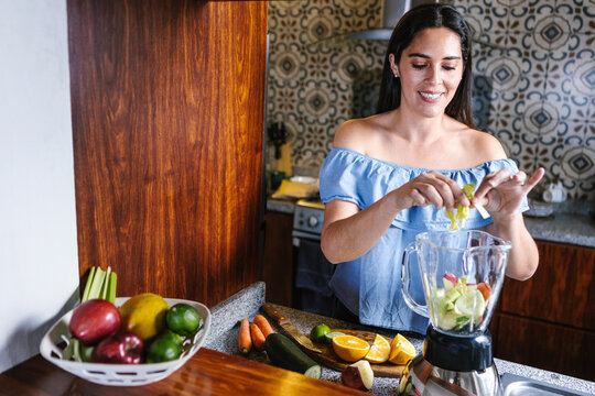 Latin Woman Making Green Smoothie Or Detox Juice In Kitchen At Home In Healthy Eating Concept In Mexico