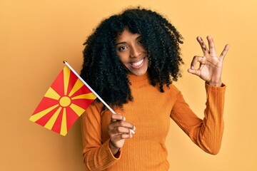 African american woman with afro hair holding macedonia flag doing ok sign with fingers, smiling friendly gesturing excellent symbol