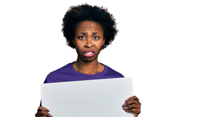 African american woman with afro hair holding blank empty banner clueless and confused expression....