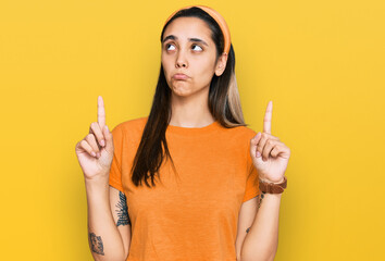 Young hispanic woman wearing casual clothes pointing up looking sad and upset, indicating direction...