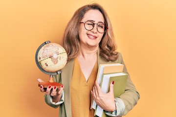 Middle age caucasian woman holding world ball and books winking looking at the camera with sexy...