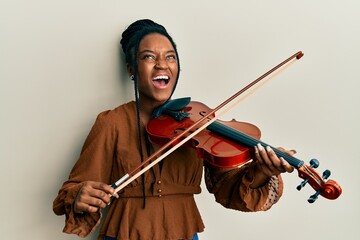 African american woman with braided hair playing violin angry and mad screaming frustrated and...