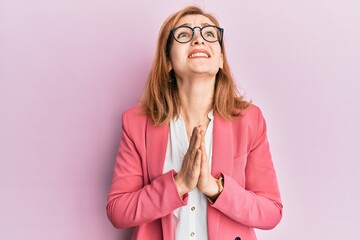 Young caucasian woman wearing business style and glasses begging and praying with hands together with hope expression on face very emotional and worried. begging.