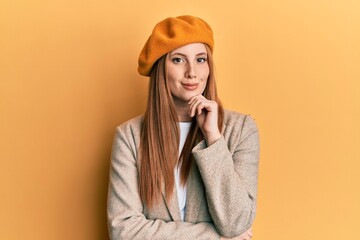 Young irish woman wearing french look with beret serious face thinking about question with hand on chin, thoughtful about confusing idea