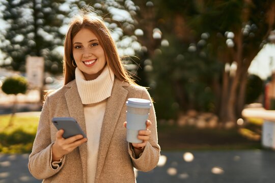 Young redhead girl using smartphone drinking coffee at the city.