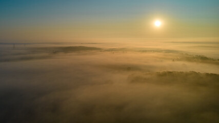 Fototapeta na wymiar In the morning at sunrise above the fog. Landscape above a village between the forests. Aerial view.